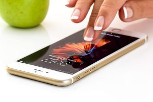 Woman touching her phone with a green fruit beside the phone.